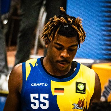 Basketballspieler mit gestreiften, gefärbten Haaren trägt ein blau-gelbes Trikot.