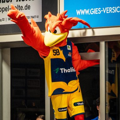 Sportliches Maskottchen in orange-blauer Kleidung, das in einen Raum hineinragt.