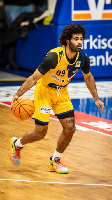 Basketballspieler mit Ball in gelbem Trikot, bewegt sich auf dem Spielfeld.