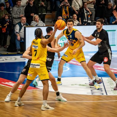 Basketballspiel mit Spielern in gelben und schwarzen Trikots auf dem Feld.