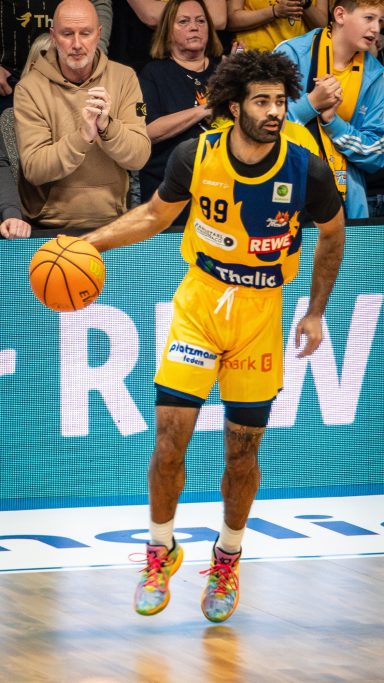 Ein Basketballspieler dribbelt den Ball, umgeben von jubelnden Zuschauern.