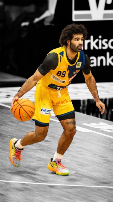 Basketballspieler dribbelt den Ball in einem gelben Trikot auf dem Spielfeld.